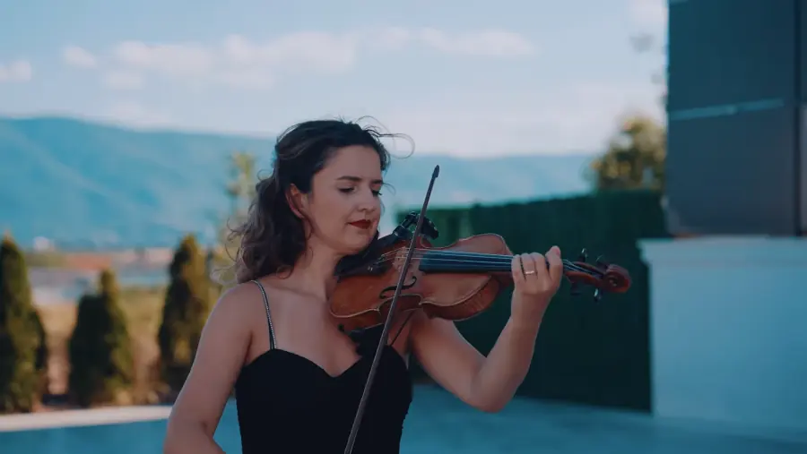 Violiniste me fustan të zi që luan në natyrë, me malet pas saj